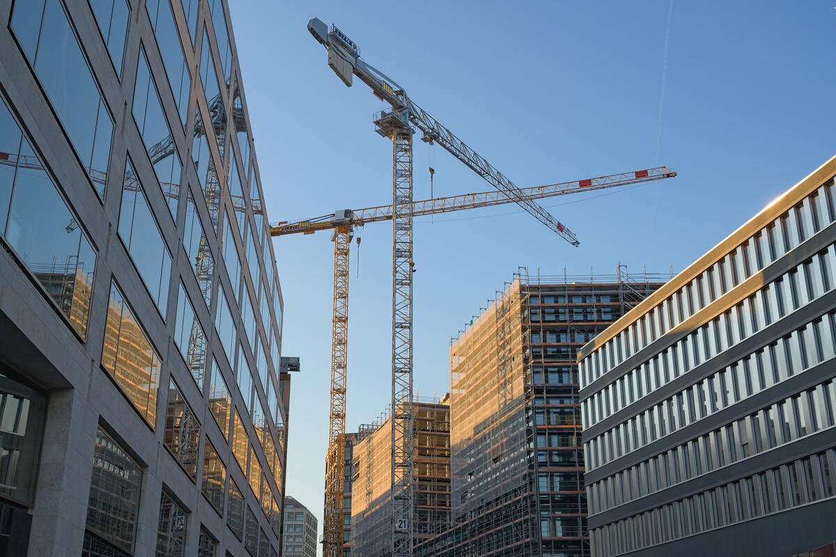 Zwei Baukräne über modernen Bürogebäuden mit Glasfassaden in einer Stadt