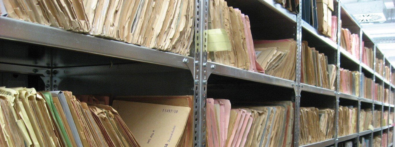Regalreihen mit zahlreichen Aktenordnern und Dokumenten in braunen und beigen Mappen, ordentlich sortiert.
