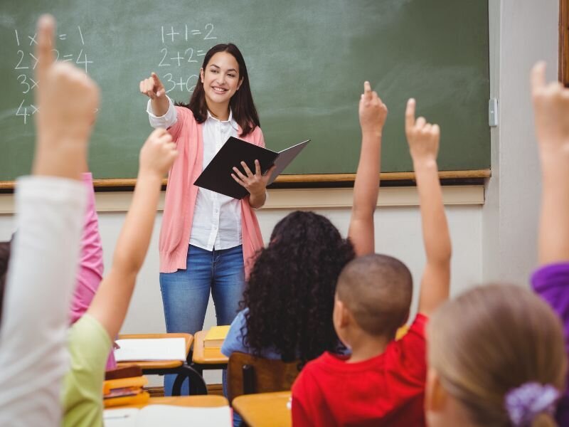 Teacher engaging students with raised hands in a classroom