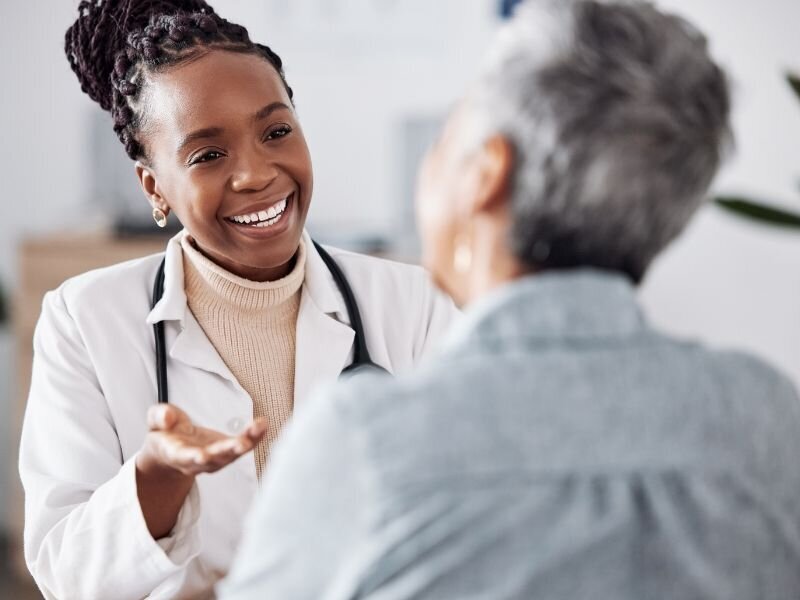 Smiling healthcare worker in white coat speaking with a patient