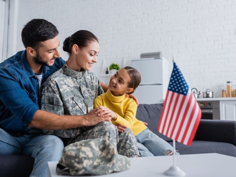 Military service member in uniform at home with family and American flag