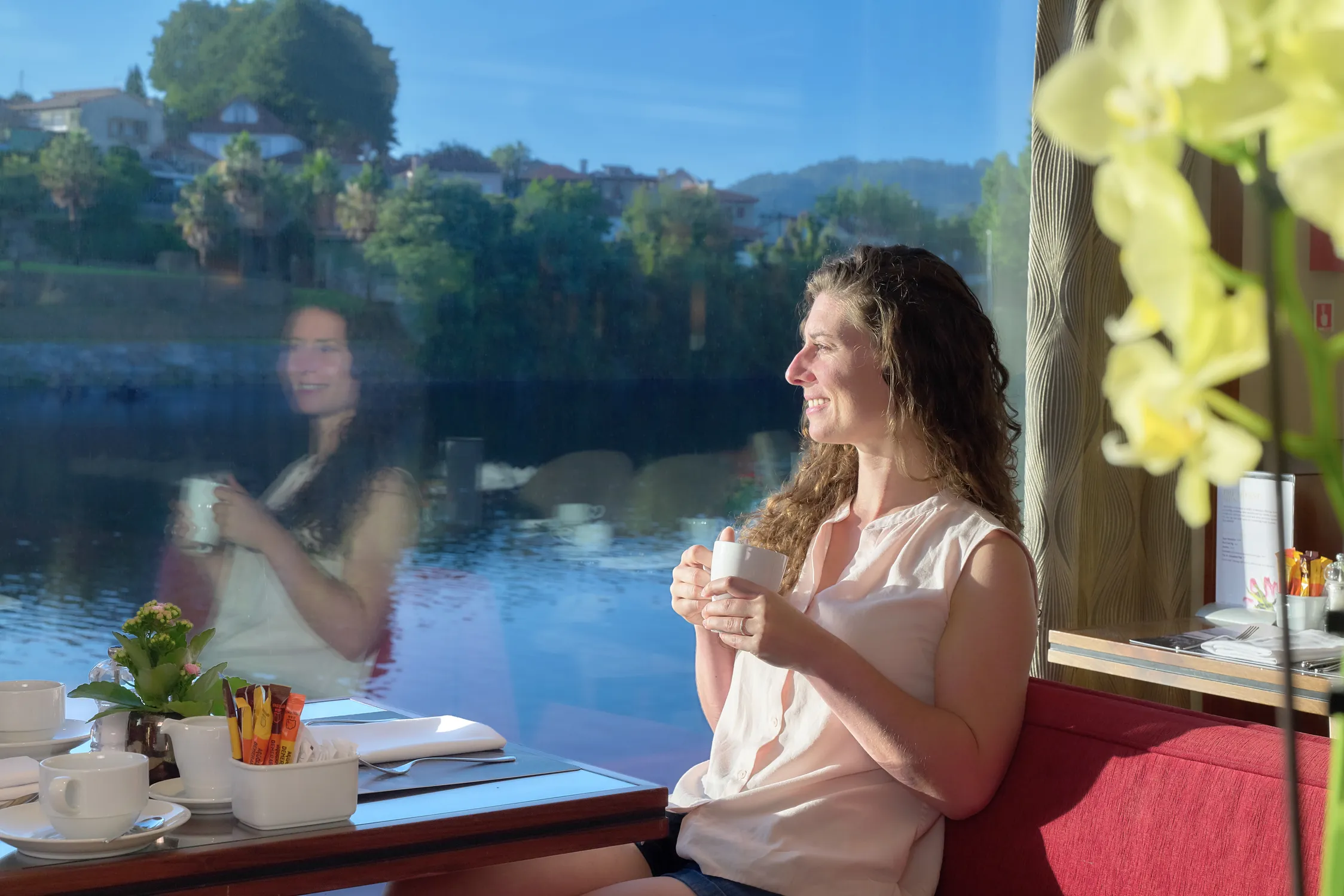 A guest on board the AmaVida in Portugal enjoying a drink while looking out at the river through the window