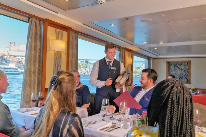Guest on board the AmaVida being served by a waiter with a view of the river in the back