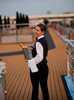 Crewmember holding drink and smiling on deck