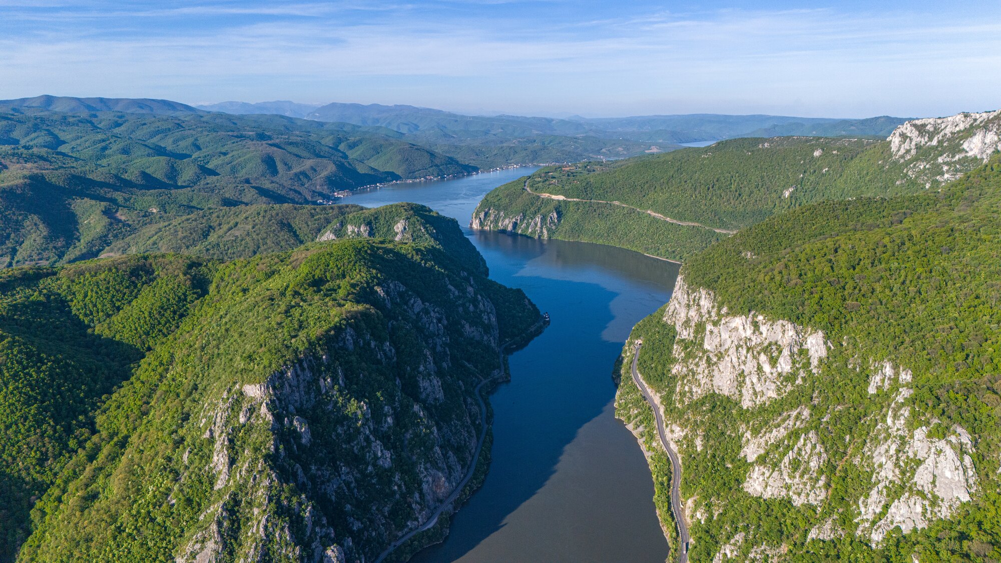 Aerial view of the Iron Gates Gorge on the Danube River, marking the border between Serbia and Romania. Towering cliffs and forested hills frame the deep canyon in the heart of the Balkans.