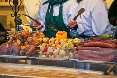 Street food stall of the Christmas market in Budapest. Christmas fair in winter. Roasted pork knuckle, Hungarian mangalica sausage, shashlik.