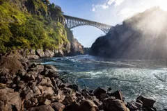The Victoria Falls Bridge crosses the Zambezi River just below the Victoria Falls and is built over the Second Gorge of the falls. As the river forms the border between Zimbabwe and Zambia