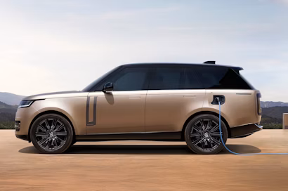 Il SUV premium color bronzo, fotografato di lato, è parcheggiato all'aperto e si sta ricaricando a una stazione di ricarica, con il cavo di ricarica inserito nel parafango posteriore.