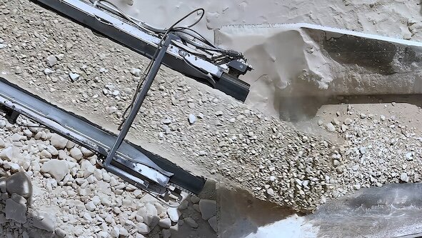  An overhead view shows a quarry with a conveyor belt transporting crushed limestone or rocks, which are being dumped into a hopper.