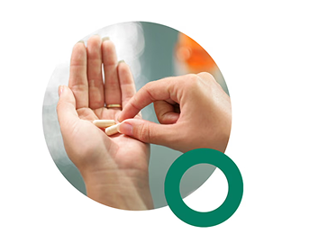 A hand holds two white capsules.