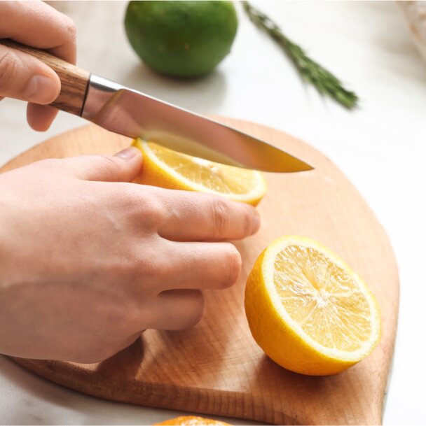 a hand holding a knife cutting a lemon in half
