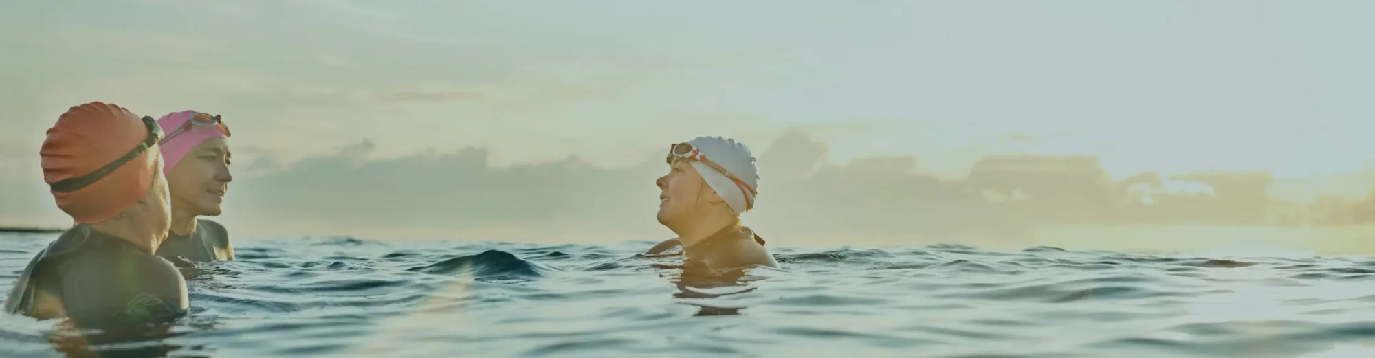 Three swimmers in the ocean at sunset