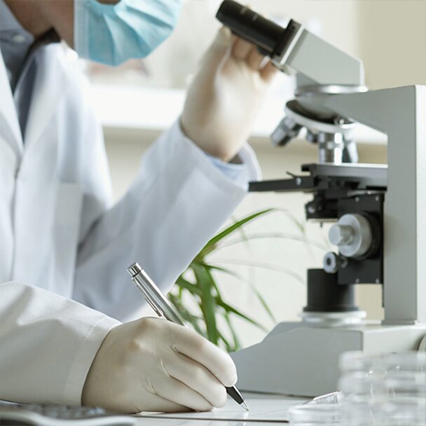 a person in a lab, looking into a microscope and taking notes