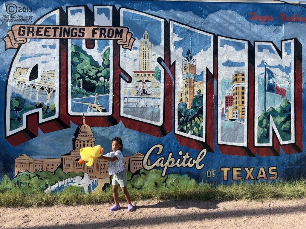 Child holding yellow Snoozimal in front of colorful Austin mural featuring iconic Texas landmarks and Capitol building