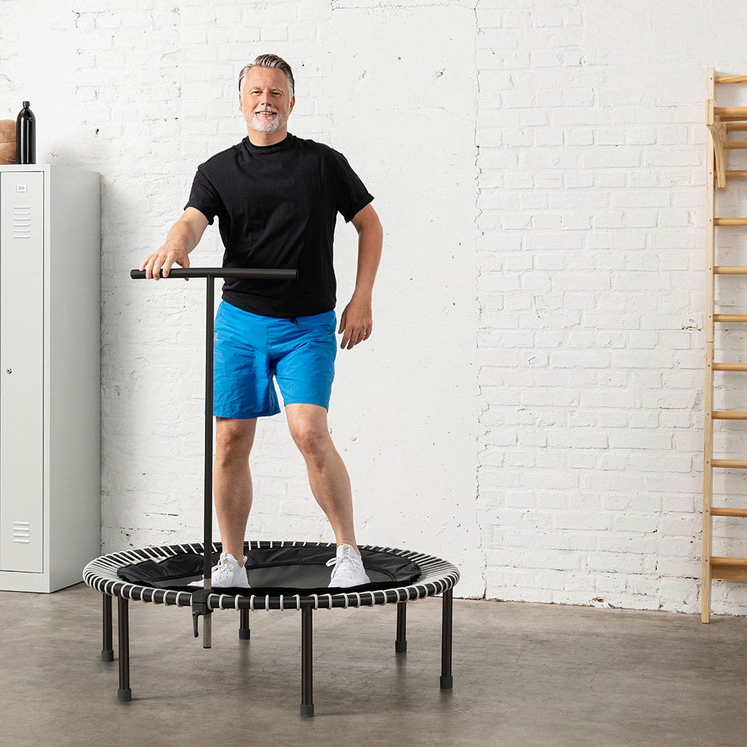 Un homme rebondit sur le trampoline bellicon avec une barre T pour plus de stabilité.