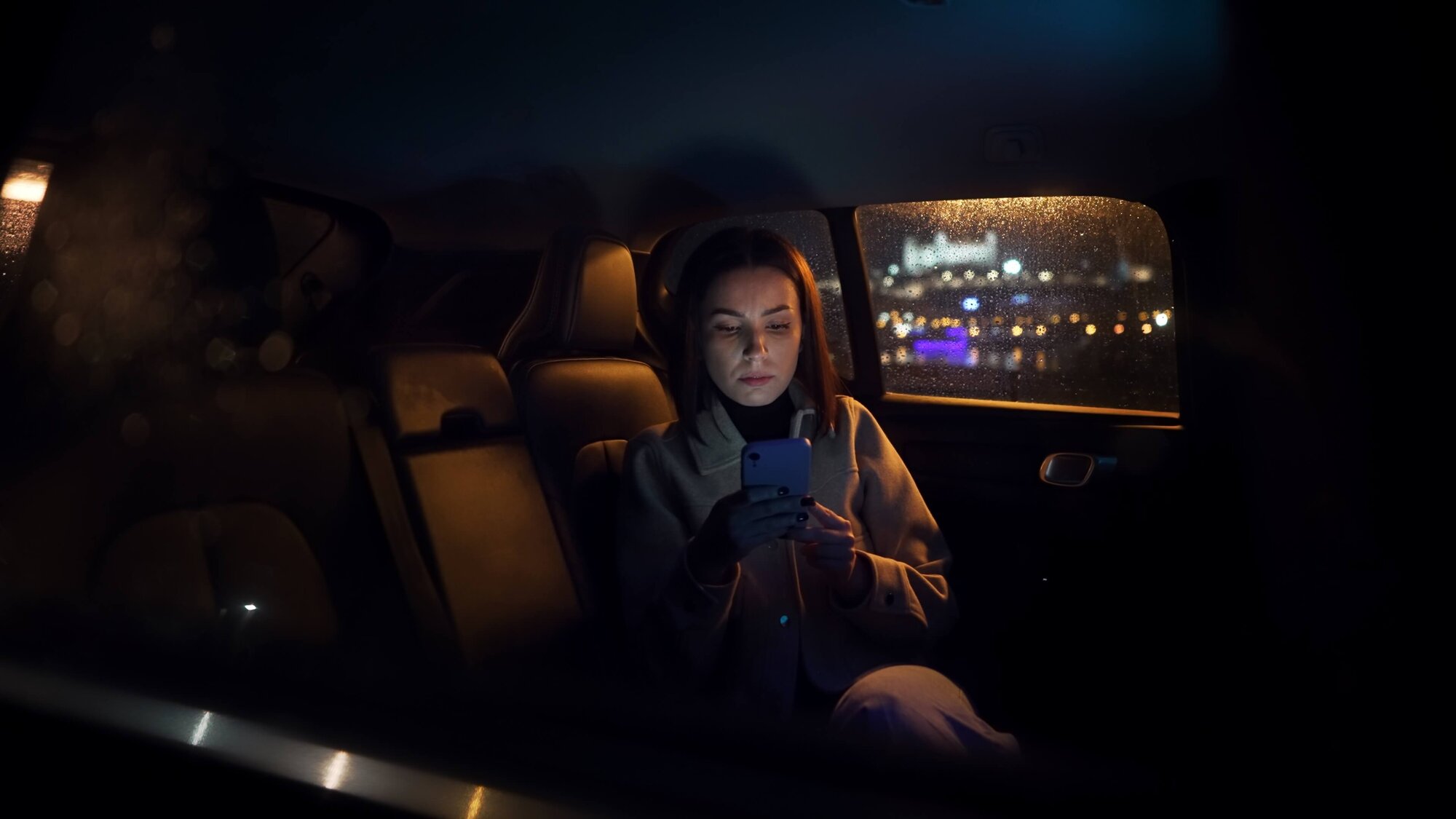 Woman sitting in backseat of a car looking at her phone.