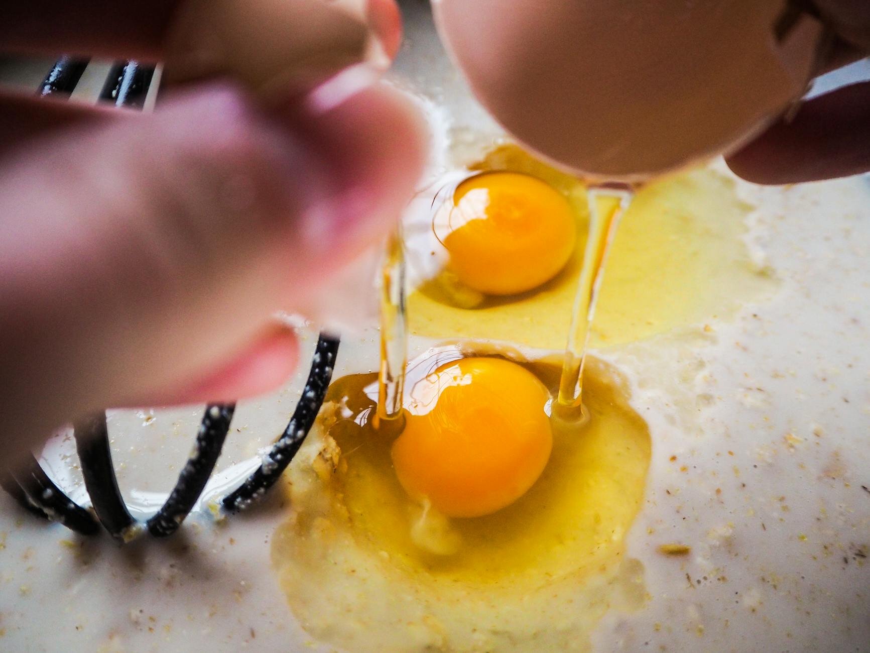 close up of person cracking eggs into bowl with whisk