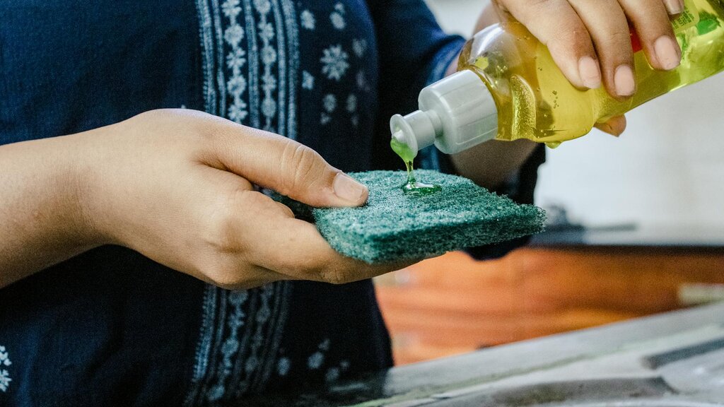 person pouring dishwashing liquid onto scourer