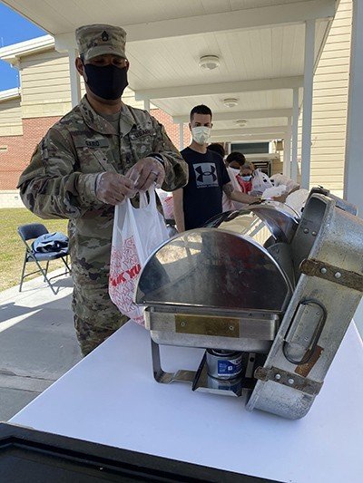 Staff Sgt. Josua Garo, 369th Composite Truck Company, Special Troops Battalion, 3rd Infantry Division Sustainment Brigade, hands off a bagged lunch to a Diamond Elementary School food service staff member April 29, 2020, on Fort Stewart, Georgia. Photo by Kevin Larson/U.S. Army.