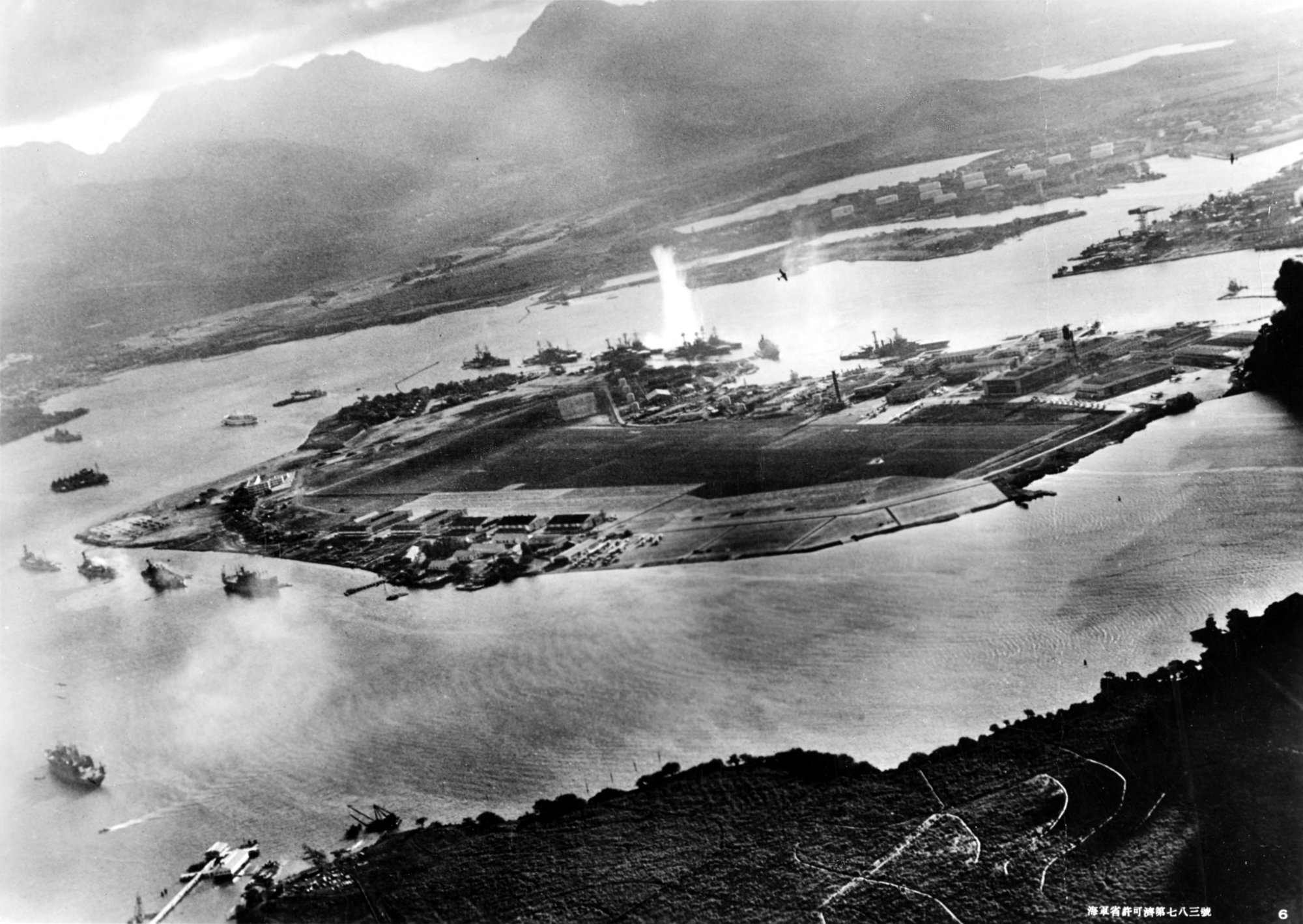 Photograph taken from a Japanese plane during the torpedo attack on ships moored on both sides of Ford Island. View looks about east, with the supply depot, submarine base and fuel tank farm in the right center distance. A torpedo has just hit USS West Virginia on the far side of Ford Island (center). Other battleships moored nearby are (from left): Nevada, Arizona, Tennessee (inboard of West Virginia), Oklahoma (torpedoed and listing) alongside Maryland, and California. On the near side of Ford Island, to the left, are light cruisers Detroit and Raleigh, target and training ship Utah and seaplane tender Tangier. Raleigh and Utah have been torpedoed, and Utah is listing sharply to port. Japanese planes are visible in the right center (over Ford Island) and over the Navy Yard at right. Japanese writing in the lower right states that the photograph was reproduced by authorization of the Navy Ministry.  U.S. Naval History and Heritage Command Photograph.