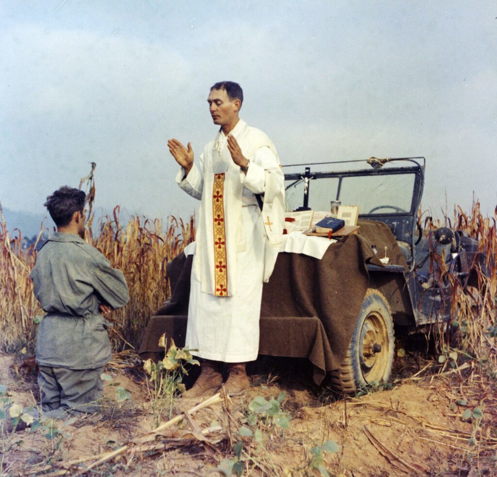 Father Emil Kapaun celebrates Mass using the hood of his jeep as an altar, as his assistant, Patrick J. Schuler, kneels in prayer in Korea on Oct. 7, 1950, less than a month before Kapaun was taken prisoner. Kapaun died in a prisoner of war camp on May 23, 1951, his body wracked by pneumonia and dysentery. Photo by U.S. Army Col. Raymond A. Skeehan, courtesy of DVIDS.