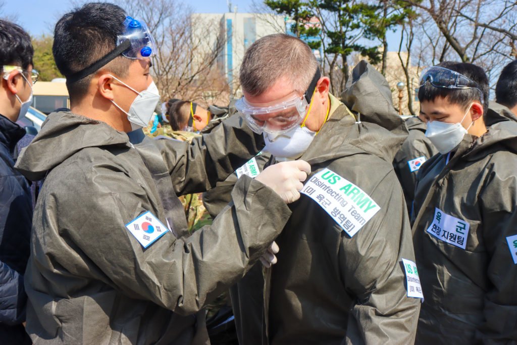 A South Korea soldier assists a U.S. Army soldier with donning personal protective equipment before sanitizing a COVID-19 infected area during a joint disinfecting operation in Daegu, South Korea, March 13, 2020. Photo by Army Spc. Hayden Hallman, courtesy of the Department of Defense.