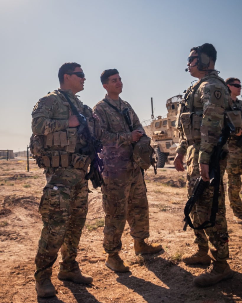 The sun beams down upon U.S. troops and Q-Wet before a mission. Its a moderate fall day for Iraq, roughly 80 degrees Fahrenheit. Everything in the area is covered in the fine dust that defines this region of Iraq. Come the change of season, Q-West will become one giant mud puddle.
