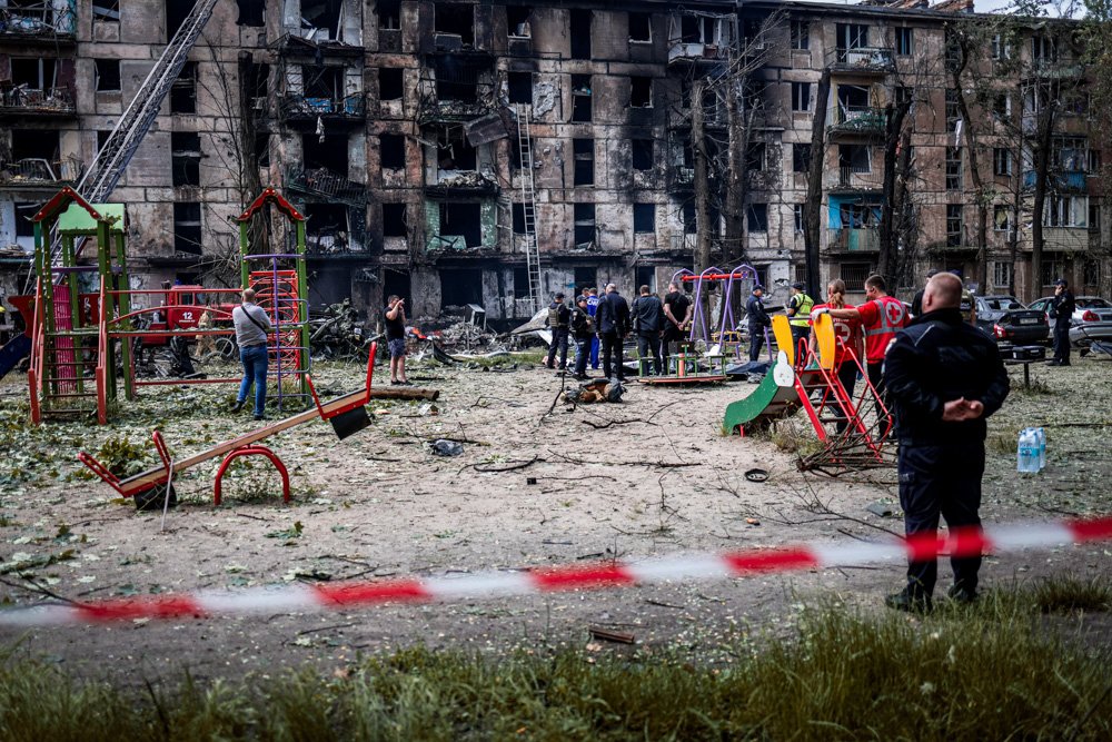 People watch the scene at a damaged multi-story apartment building caused by the latest Russian rocket attack