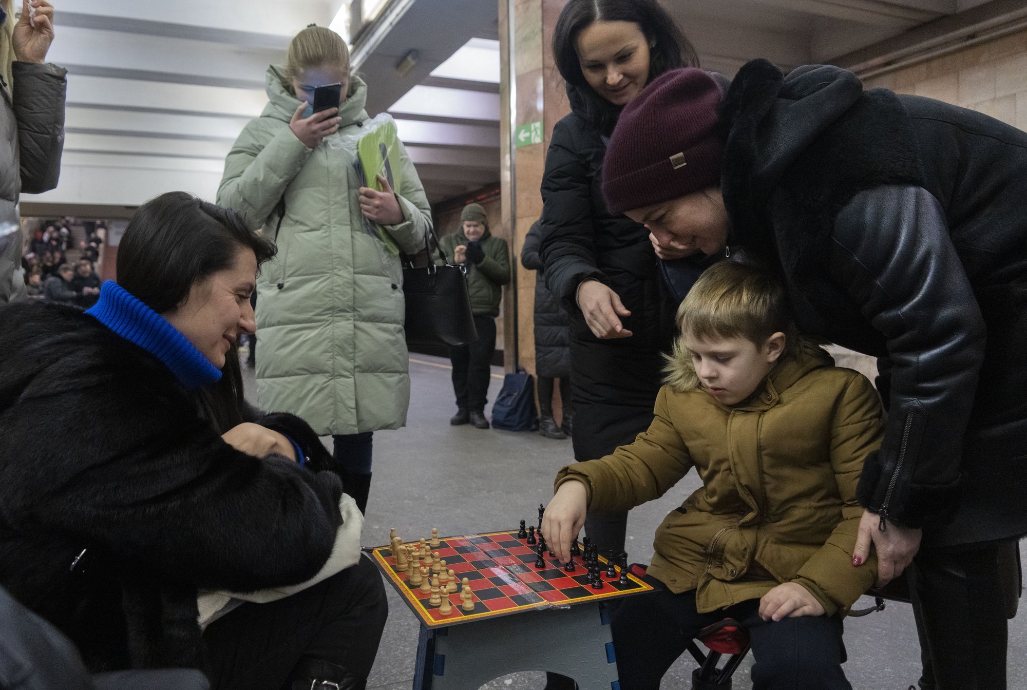 A boy and a woman play chess as other people watch in a subway station being used as a bomb shelter during a Russian rocket attack in Kyiv, Ukraine, Friday, Feb. 10, 2023. (AP Photo/Efrem Lukatsky)