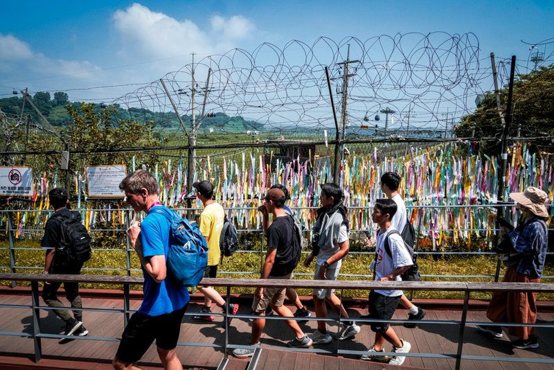 Visitors pass by a wire fence decorated with ribbons written with messages wishing for the reunification of the two Koreas.