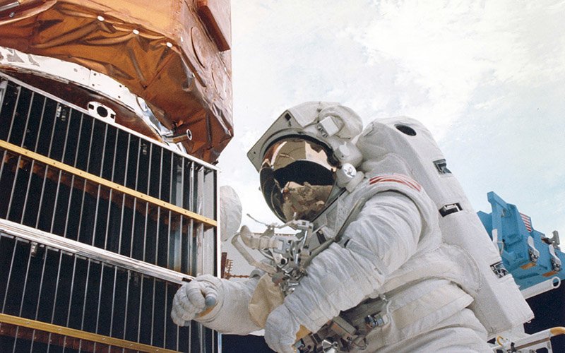 An astronaut works on the Solar Max satellite in 1984.  During repairs inside the Space Shuttle, the astronauts discovered that several metal louvers and thermal blankets were damaged by debris. NASA photo.