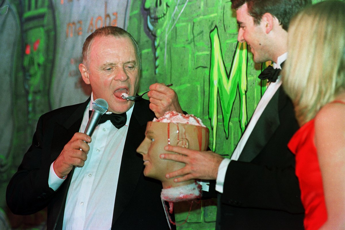 British actor Anthony Hopkins (left) has a bite to eat during a roasting in his honor with seniors Ben Forkner (center) and Suzanne Pomey (right) after being named Man of the Year by the Hasty Pudding Theatricals at Harvard University on Feb. 15, 2001, in Cambridge, Mass.  Hopkins played the role of a murdering psychopath in “Silence of the Lambs” and “Hannibal”, scaring the wallets off of North American movie goers. Photo by John Mottern/AFP via Getty Images.
