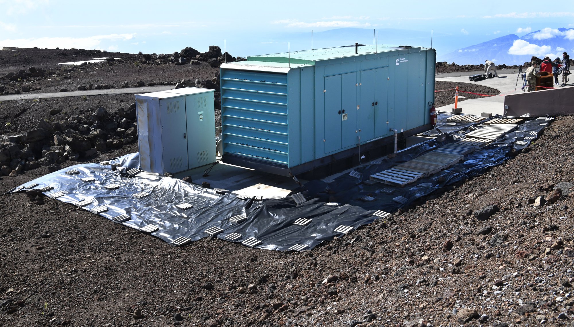 A container holding a backup generator and fuel tank sits amid black tarp covering a concrete pad and surrounding soil at Haleakala High Altitude Observatory in Hawaii on Feb. 6, 2023, where an estimated 700 gallons of diesel fuel spilled in late January. (Matthew Thayer/The Maui News via AP)