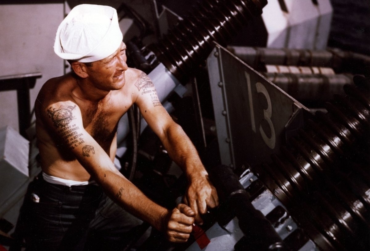 Battleship Missouri  Gunner’s Mate 2nd Class Charles J. Hansen working on a 40mm quad machine gun mount, during the battleship’s shakedown period, circa August 1944. His tattoos pay homage his shipmates lost on the heavy cruiser Vincennes in the Battle of Savo Island on 9 August 1942, part of the Guadalcanal campaign.  US Navy photograph, now in the National Archives.