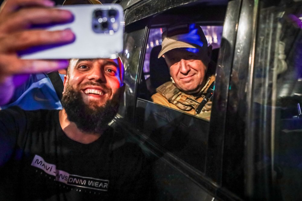 Yevgeny Prigozhin, the owner of the Wagner Group military company, right, sits inside a military vehicle posing for a selfie photo with a local civilian.