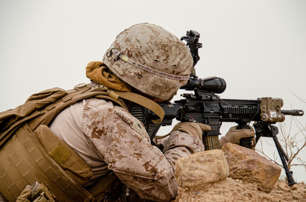 A U.S. Marine looks through the optics of his rifle at a uniformed Iraqi on a distant hill during a patrol of Al Taqqadum Airbase not long after Camp Taji was hit with rockets in March. The Marines shared the base with members of Kataib Hezbollah, an Iranian-backed Iraqi militia that has periodically rocketed American troops across the country. Photo by Kevin Knodell/Coffee or Die.