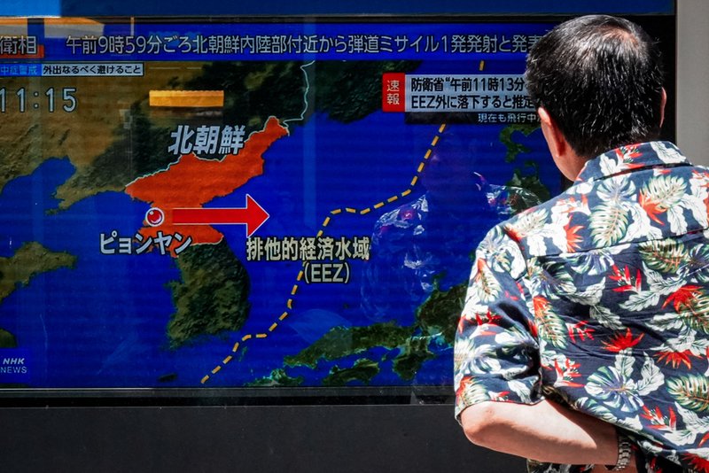 A man stands along a sidewalk to watch a TV showing a news program on North Korea's missile launch.