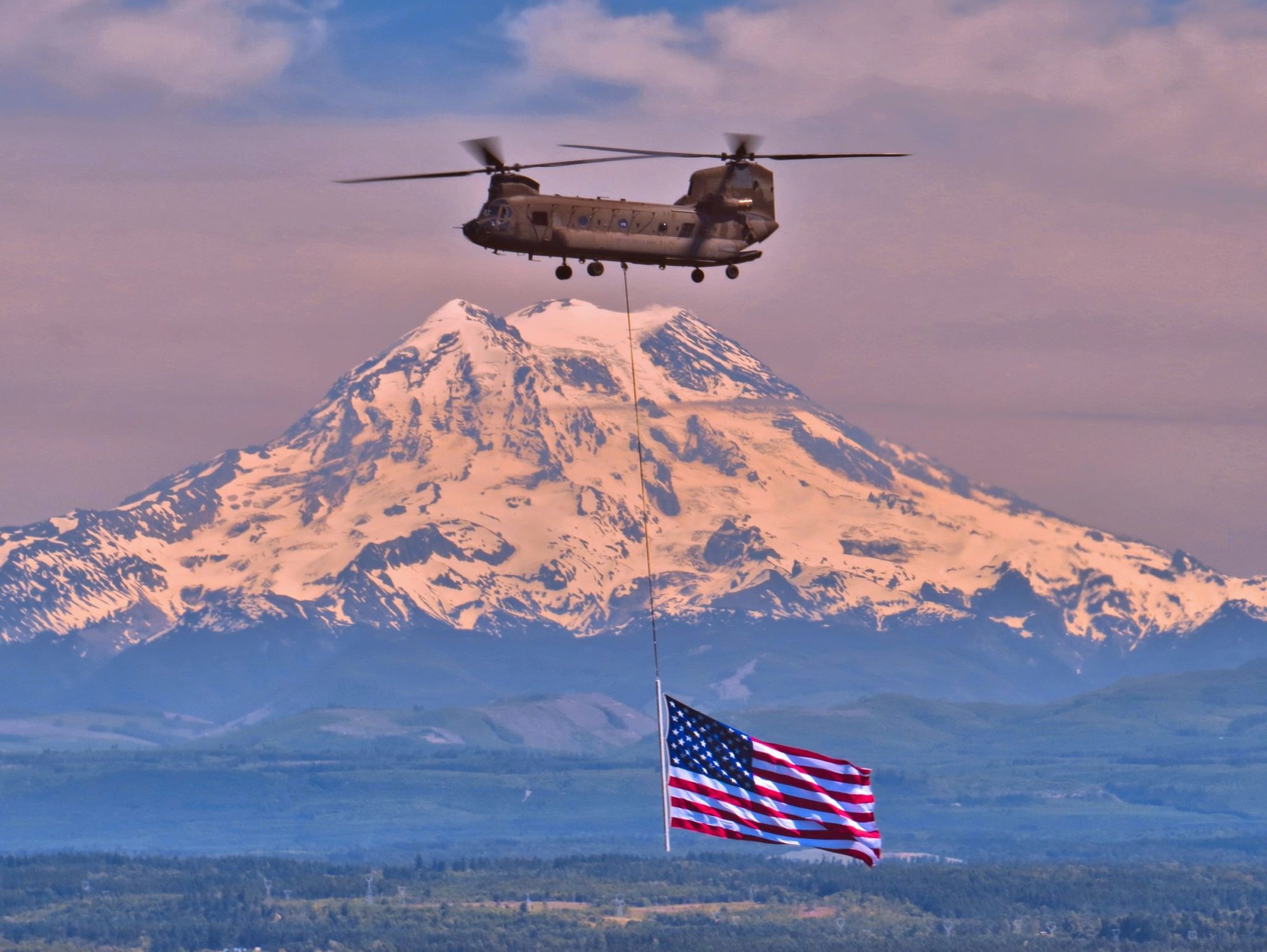 CW4 Tim Reeves and CW2 Kevin Crisp, 1-168th GSAB, Washington National Guard, perform a "flag drag" high above Puget Sound on their way to Gas Work Park in Seattle as part of the Seattle Seafair 4th of July celebration. (Photo by SFC Adolf Pinlac, D Co. 1/168th GSAB)