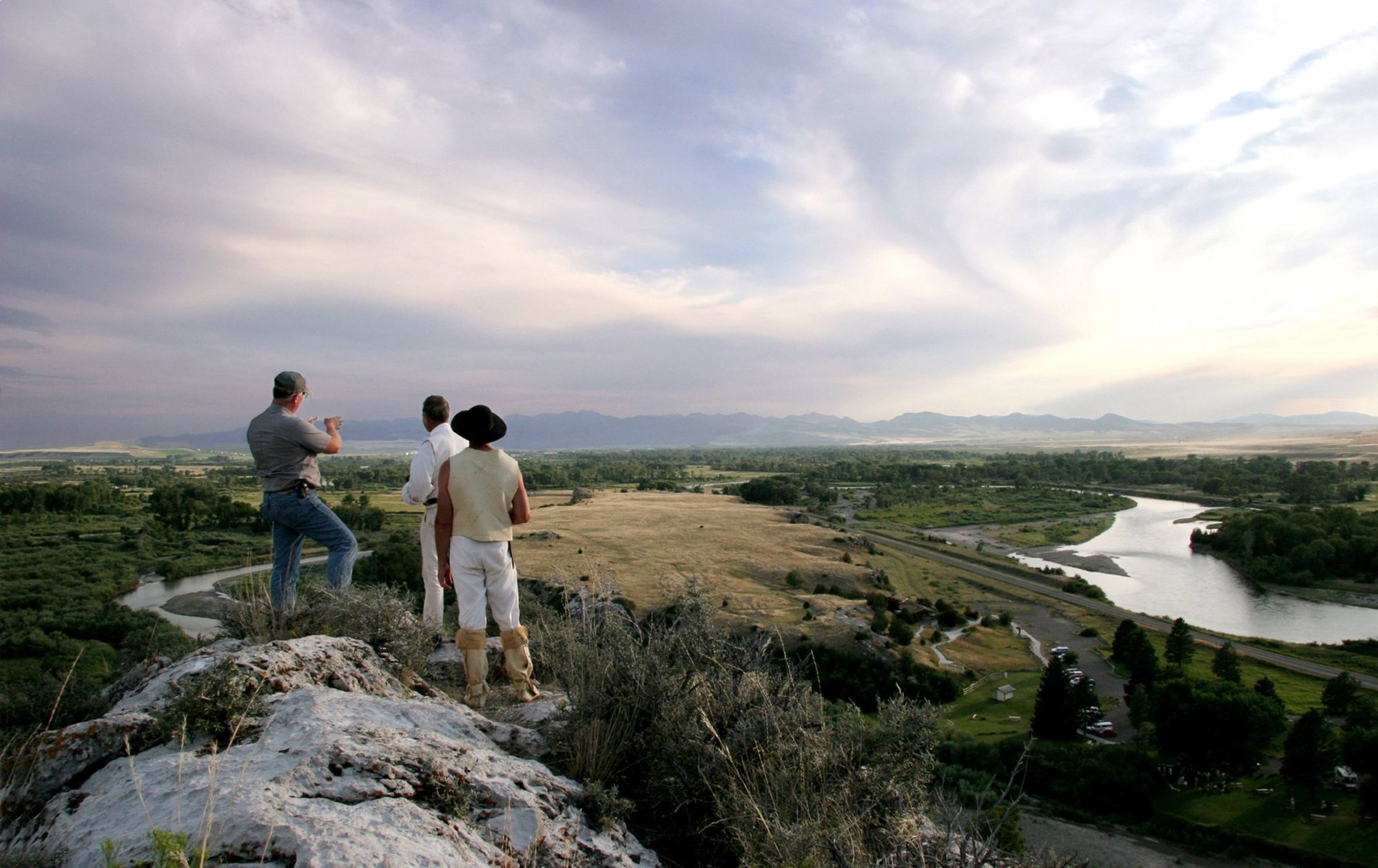 Headwaters State Park Manager Ray Heagney, left, gives a tour of the landscape from Lewis Rock on the evening of July 21, 2005. The combined Madison and Jefferson rivers, to the lower right, will soon be joined by the Gallatin River, to the left, to form the Missouri River in this primitive park near Three Forks, Montana. Heagney and park staff provided tours from the prominent rock, named after Capt. Meriwether Lewis, on the 200th anniversary of the Lewis and Clark Expedition passing through Three Forks. Photo courtesy of the National Parks Service.