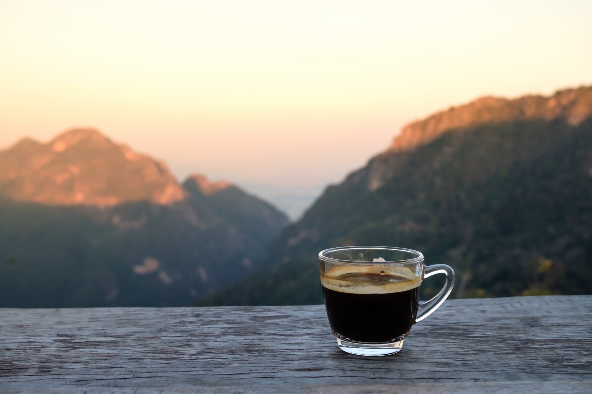 Hot americano coffee on wooden table with mountain view in the morning. Adobe Stock photo.