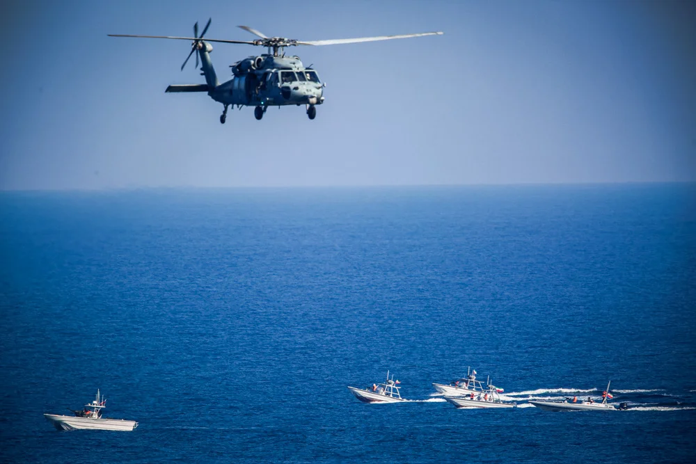A U.S. MH-60 Seahawk helicopter flies over Iranian Revolutionary Guard patrol boats in the Strait of Hormuz 