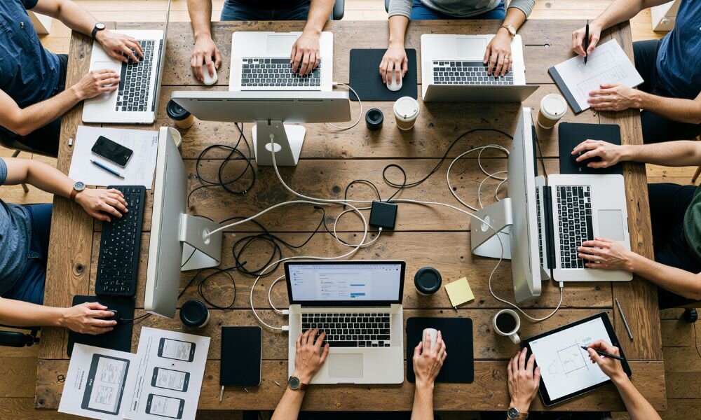 Team working together around a shared desk with laptops and tablets, illustrating the coordinated effort expected from a strong software development partner.