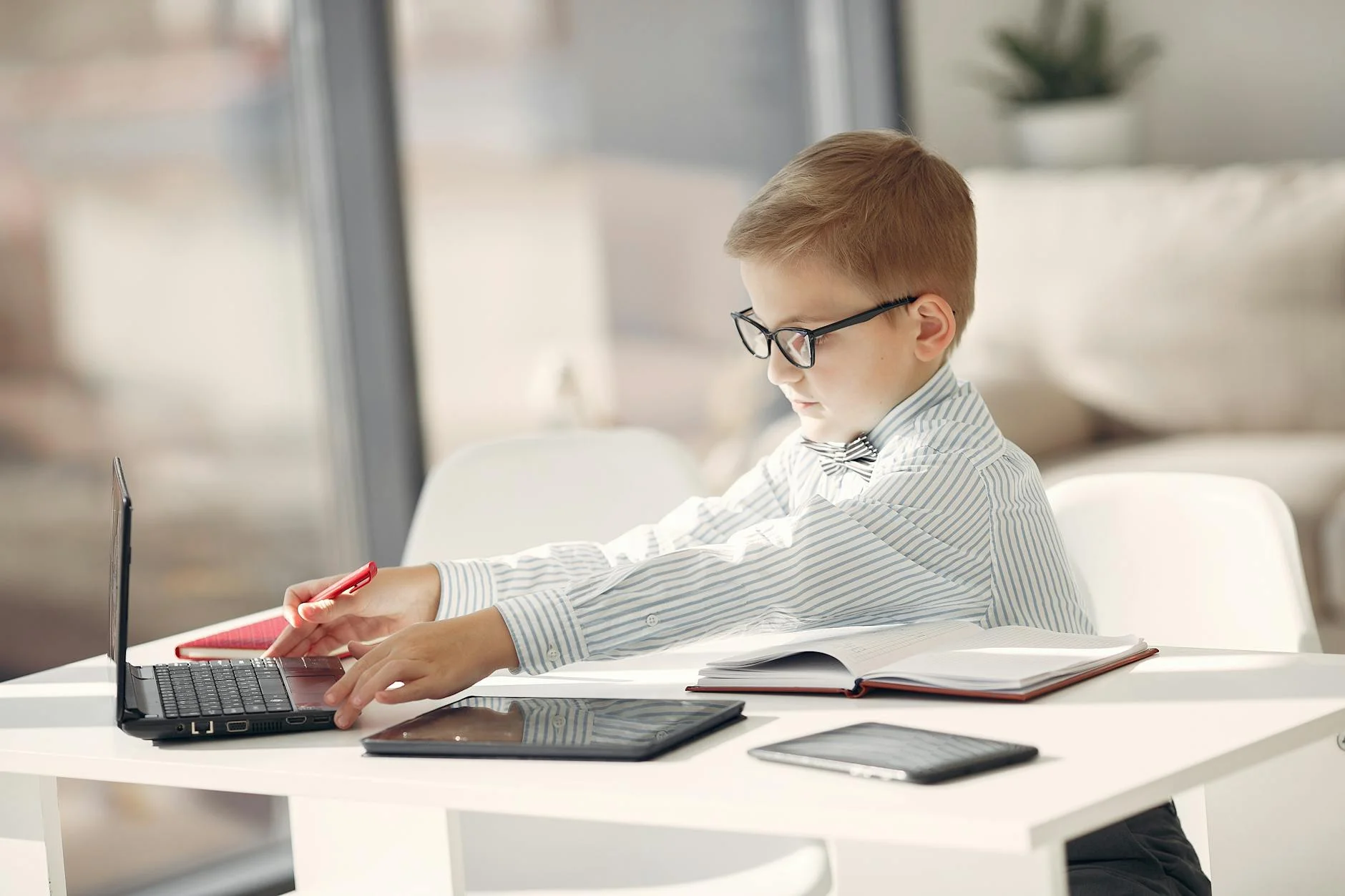 A boy with glasses working intently on a laptop, surrounded by tech devices, symbolizing early skill development in software engineering