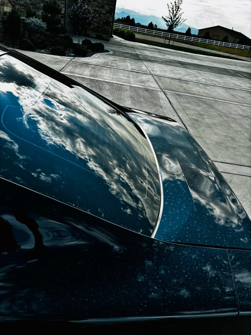 Black car rear glass and trunk reflecting a cloudy Colorado sky