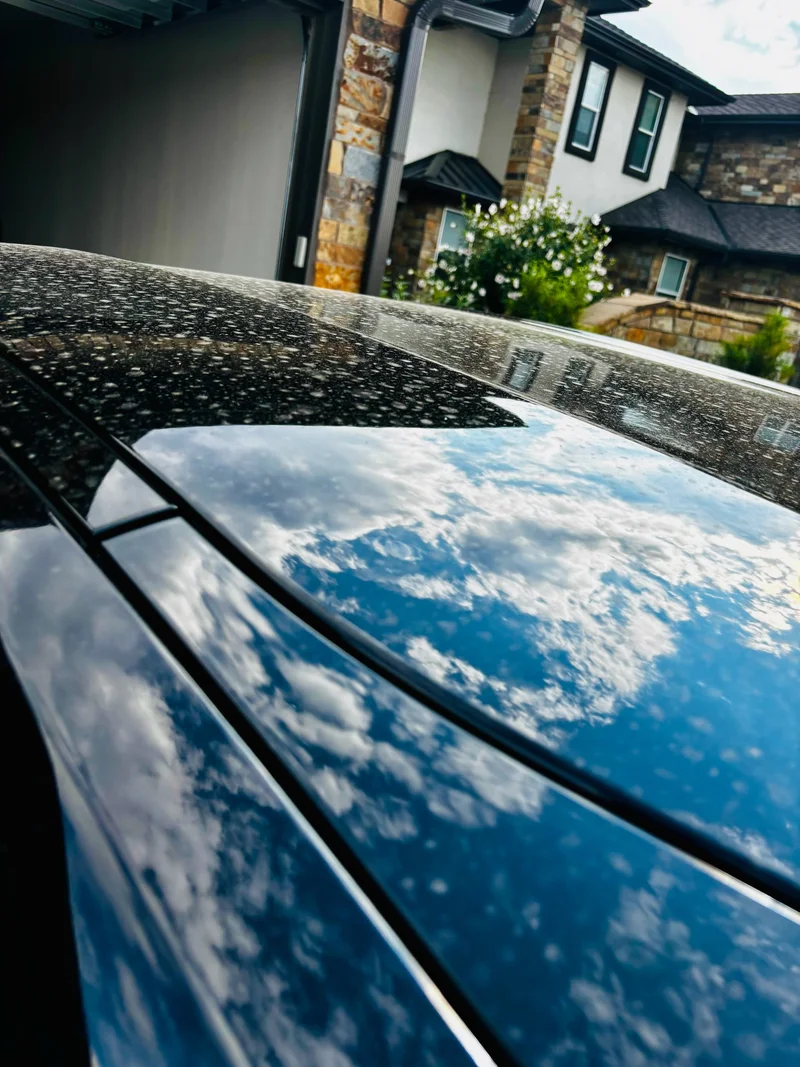 Black car roof showing water beading and a mirror-like sky reflection