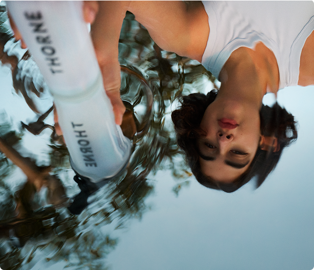 An upside down view of woman holding a transparent Thorne water bottle