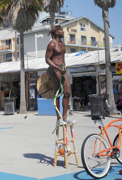 A naked black dude holding two snakes dancing