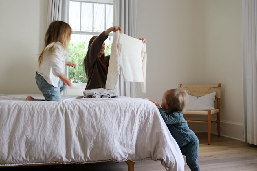 Mom folding laundry on bed with kids