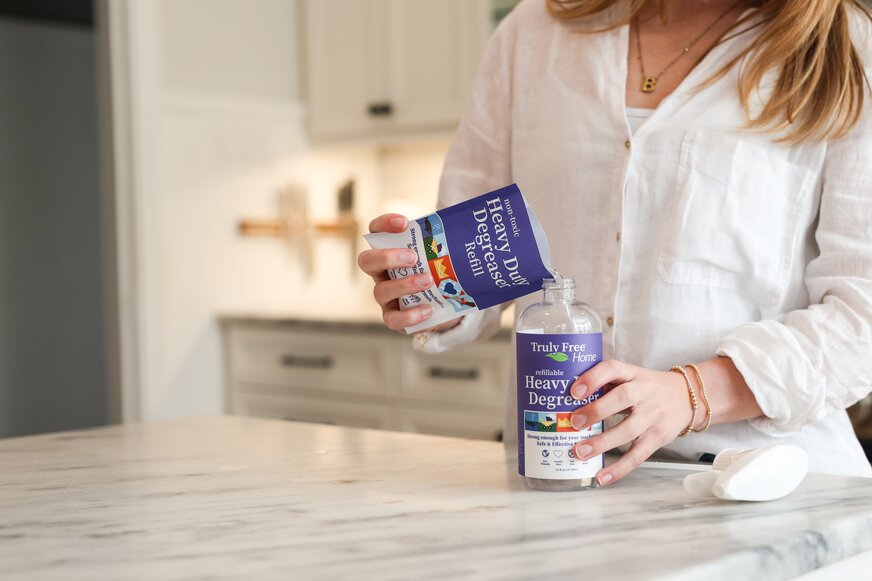 Woman refilling Truly Free Home Heavy Duty Degreaser bottle. 