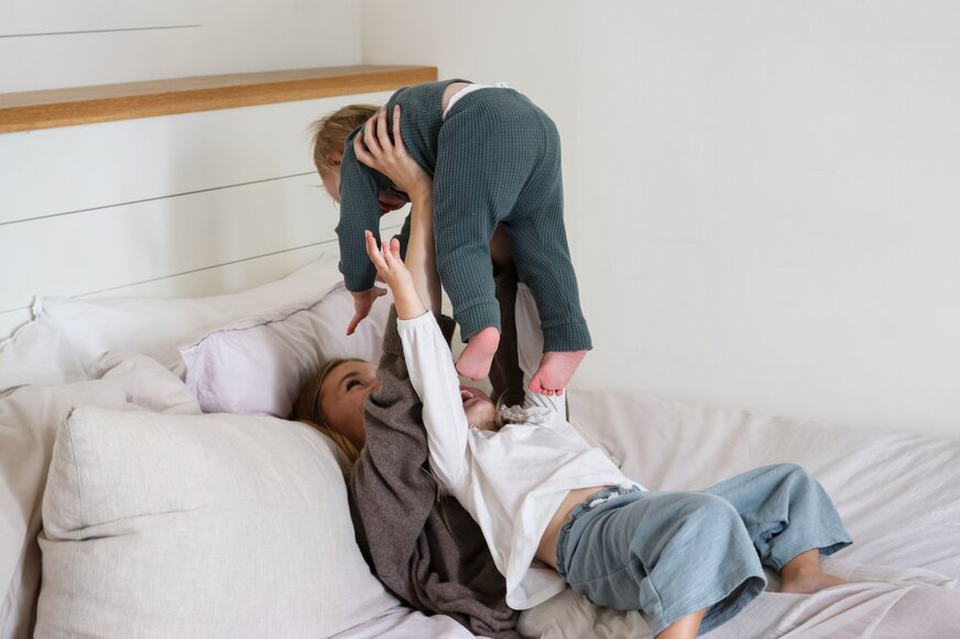 Mom and toddlers playing on bed.